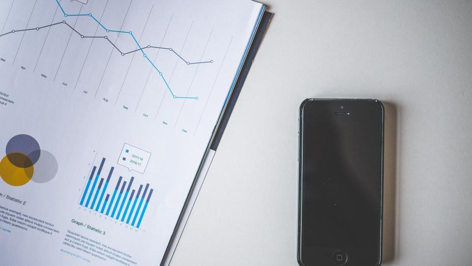 Printed marketing report showing line and bar charts beside a smartphone