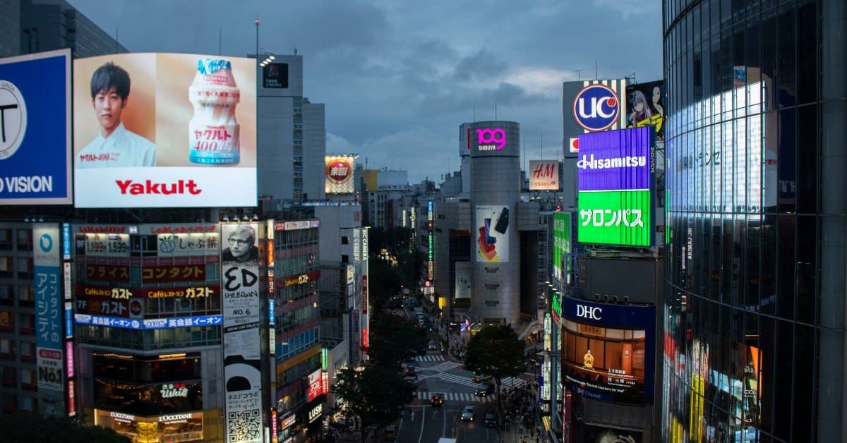 City street at dusk lined with illuminated advertising billboards and digital screens, representing the scale of paid media spend