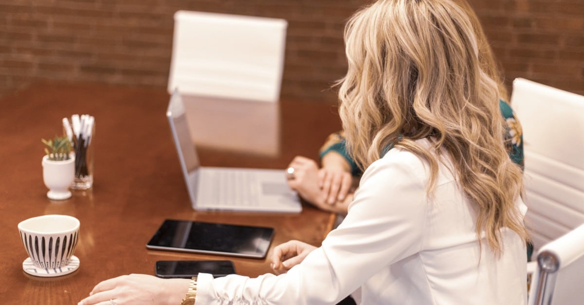 Marketer working at a laptop with a tablet and notes on the desk beside her