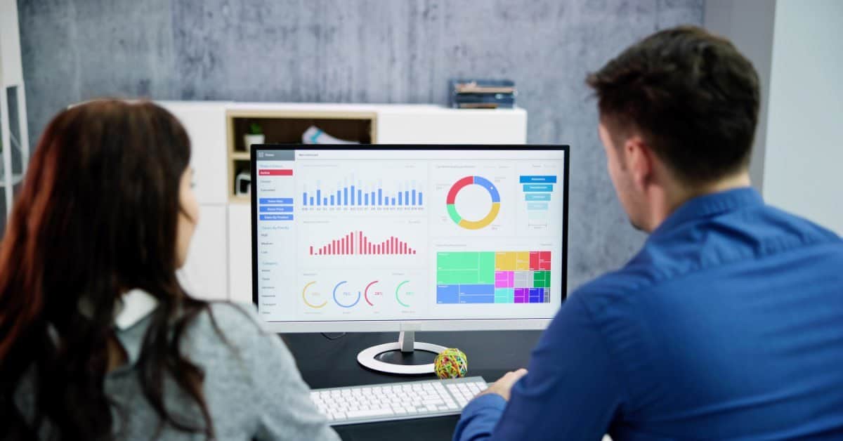 Two marketing professionals reviewing a campaign analytics dashboard on a desktop monitor