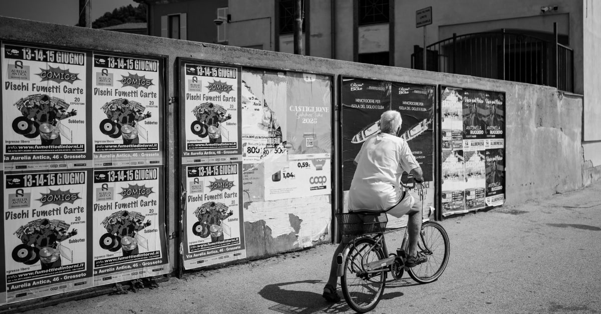 A wall of repeated identical printed posters as a cyclist rides past