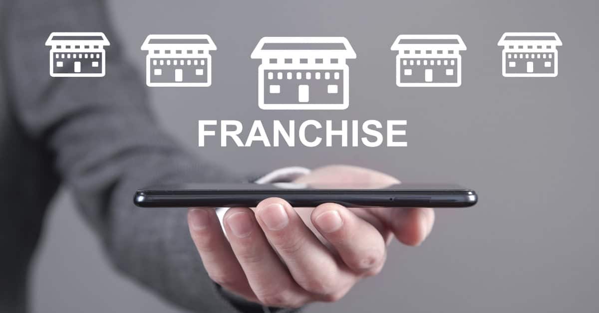 Franchise storefront icons floating above a smartphone held in one hand